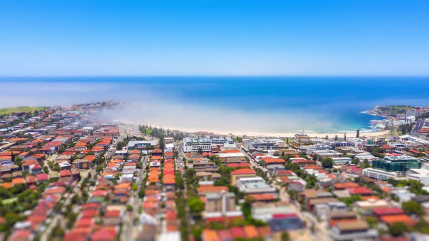 Aerial view of a coastal city with dense neighborhoods stretching toward a bright blue ocean