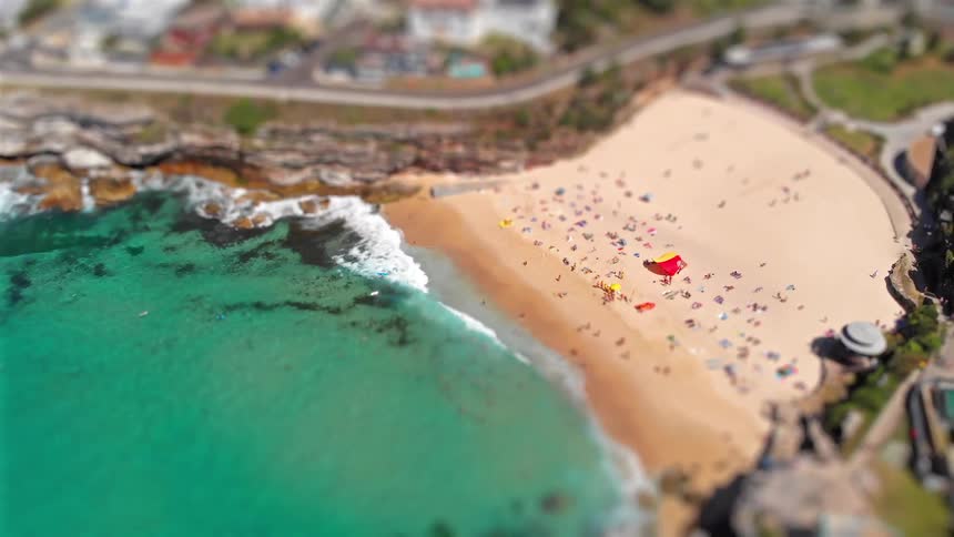 Aerial view of a beach with sandy shoreline occupied by beachgoers and greentoned sea along the rocky coast