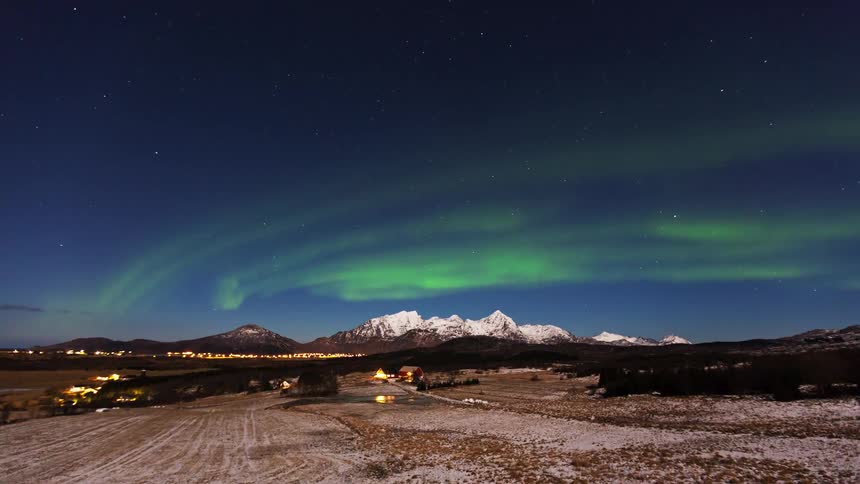 Lights glow in a mountainside community as the northern lights illuminate the sky