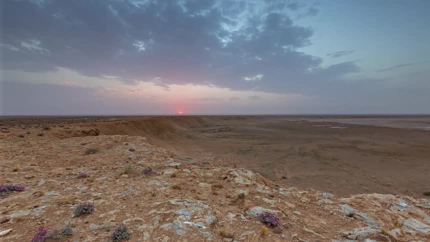 The sky transitions from golden orange to deep purple over a vast rocky desert landscape