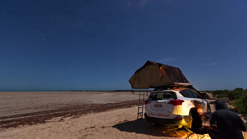 Two people camping outdoors in the desert by their car at night