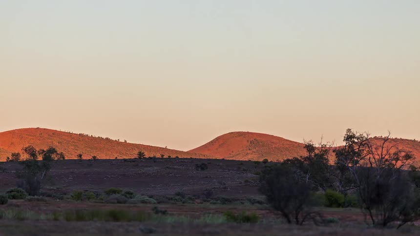 Full moon sets over the mountains and sunlight shines over the desert