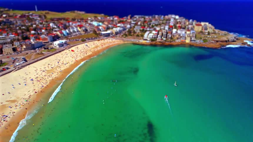 A crowded beach with vibrant turquoise water stretches alongside a coastal town