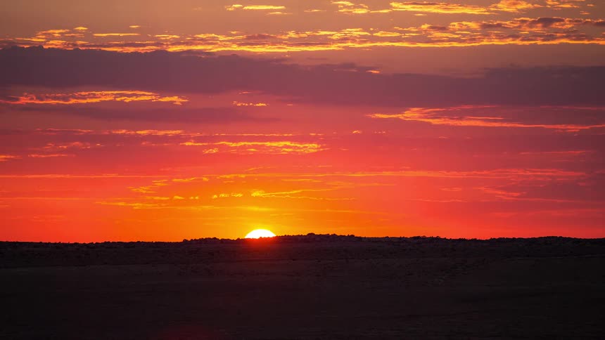 A vibrant sun rises over a dark desert horizon transitioning from deep red to brilliant gold