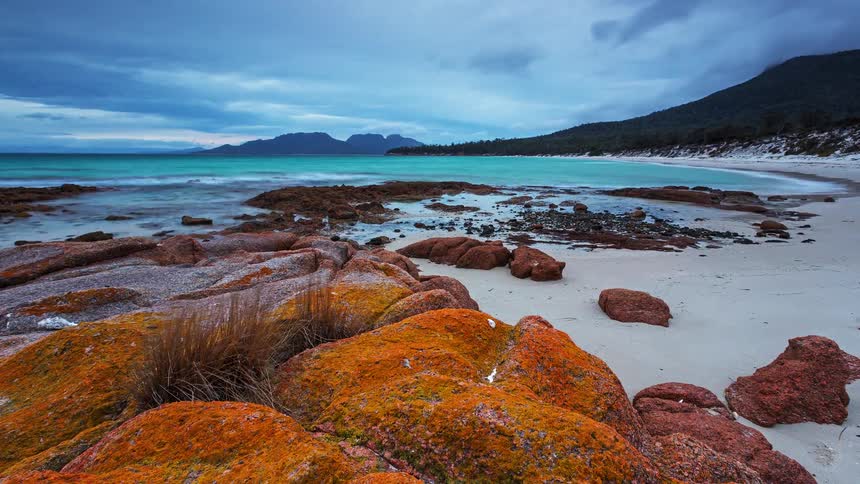 A rocky island beach with waves hitting the shoreline as the day turns from bright to dark and cloudy