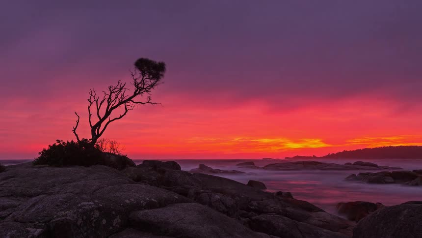 Waves move onto a rocky shore under a red sky