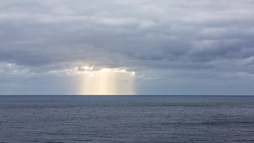 Rays of sunlight shine through clouds over the water pouring rain