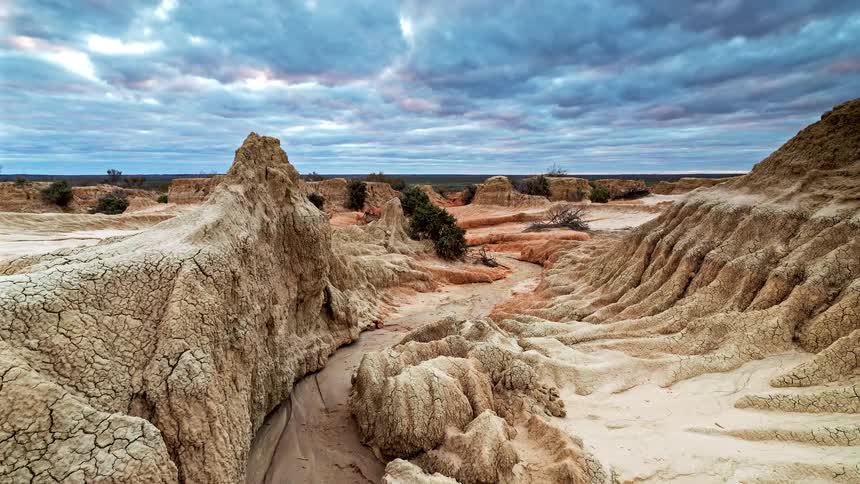 Shifting clouds and changing light pass over unique eroded rock formations in a desert landscape at sunset