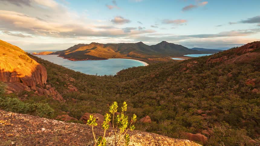Golden sunset light transitions into twilight over a crescent shaped bay and forested mountains