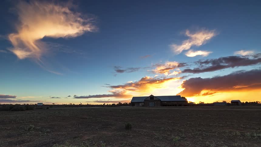 Open field with an isolated rural building on the horizon beneath an evening sky with illuminated clouds