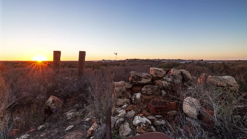 Sunrise over an arid rural landscape with stacked stones low vegetation and fence posts