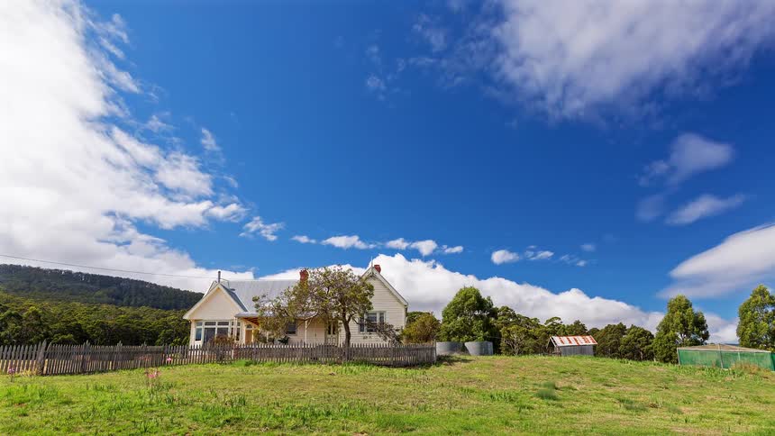 House in the country with a picket fence as trees move in the wind