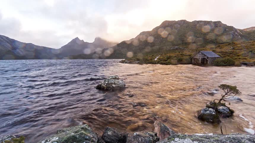 A rocky lakeside on a rainy day with a hut on the bank at midday
