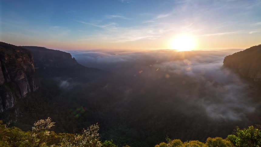 Clouds roll in low and fill a canyon as the sun rises