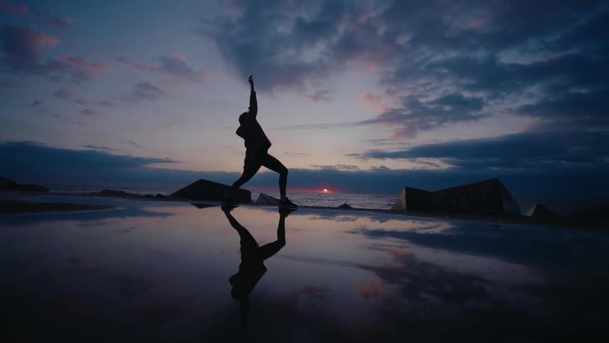 Man standing along the coast stretching and doing yoga exercises with his reflection on the wet ground