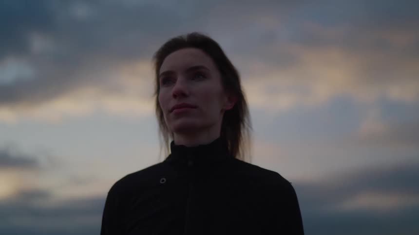 Woman outdoors with a neutral expression under a cloudy sky at dusk