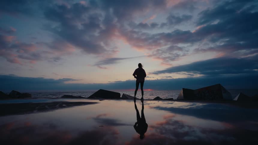 A woman jogger runs on a beach and stops to look at the sky