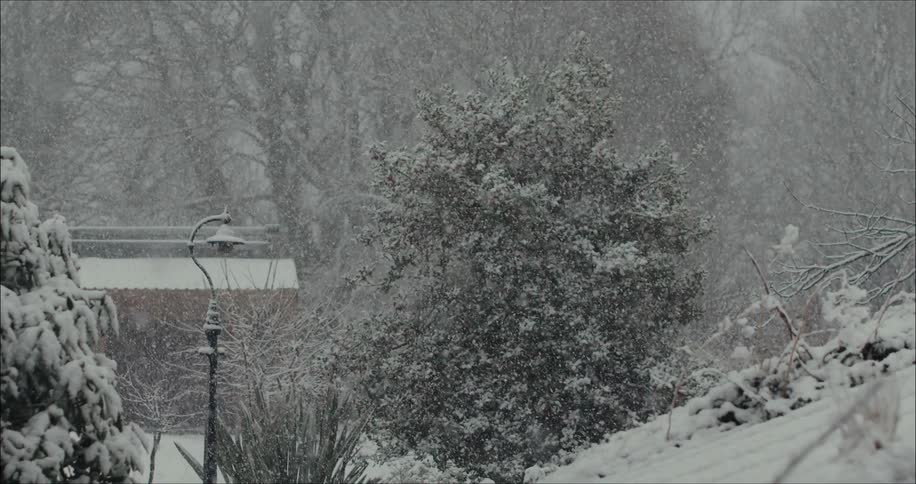 Snow slowly falls from the sky and covers the ground around a building