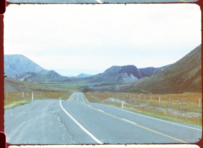 Paved rural road crossing an open valley with surrounding hills under a clear sky