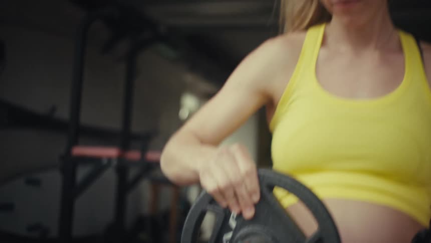 A woman in a yellow top takes off a black ten pound weight plate inside a gym