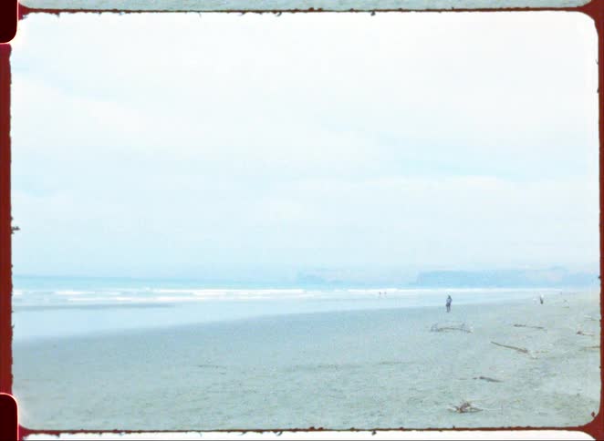 Wide beach with an expansive sandy shore gentle waves and a person walking in the distance under a clear sky