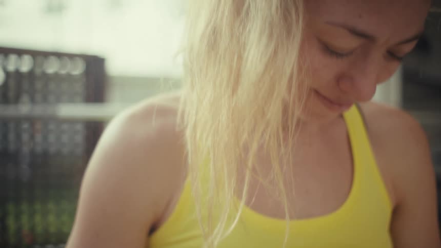 A young pregnant woman sitting on a gym bench rubbing her arms over her baby bump and smiling at midday