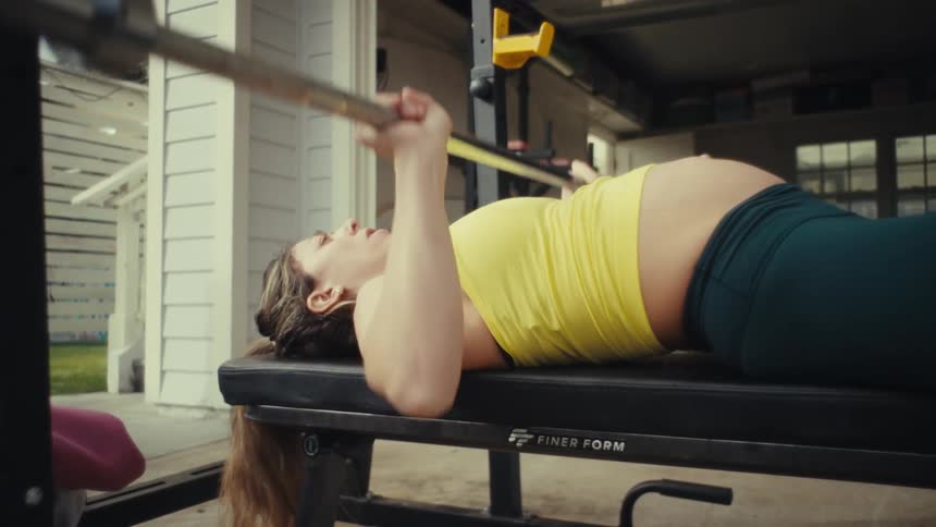 Pregnant woman lying on a bench performing a barbell bench press in a workout setting