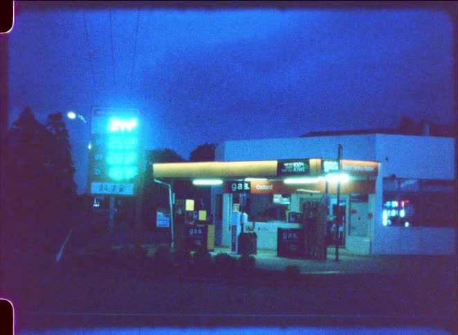 Gas station illuminated at night with fuel pumps price sign and surrounding roadway