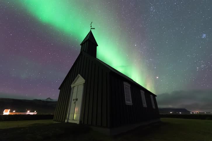 Wooden church in a rural area beneath the northern lights and a starry night sky
