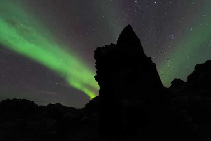 Rock formation in silhouette beneath green northern lights and a starry night sky