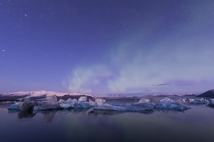 Aurora borealis partially fills the sky above icebergs and a snowy coast