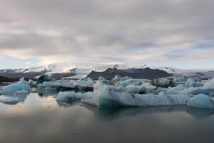 Floating ice blocks in a glacial lake with snowcovered mountains in the background under a cloudy sky