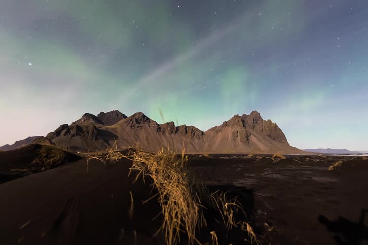 Mountains beneath the northern lights with dry grass in the foreground at night