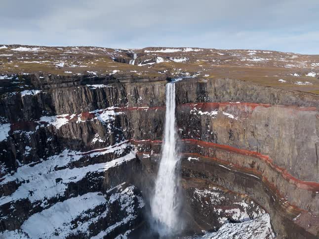 Waterfall plunging from a rocky cliff into a canyon with snow accumulated on the slopes