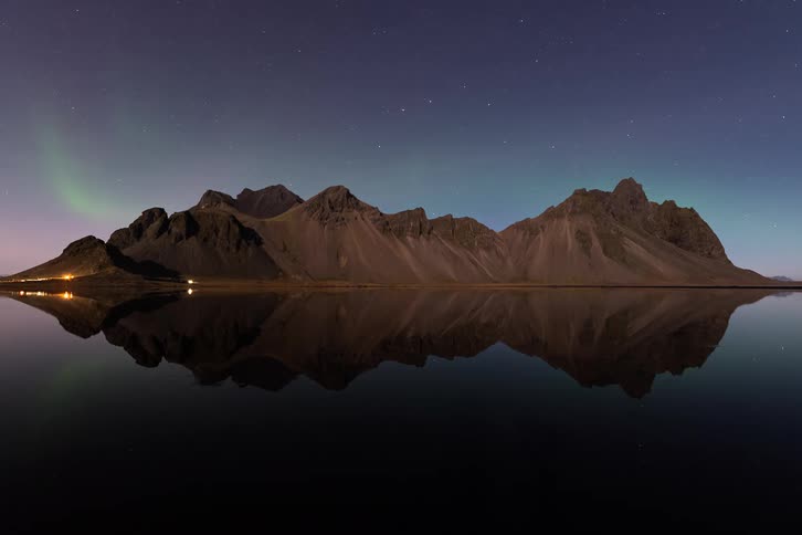 Mountain range reflected in a calm lake beneath a starry night sky