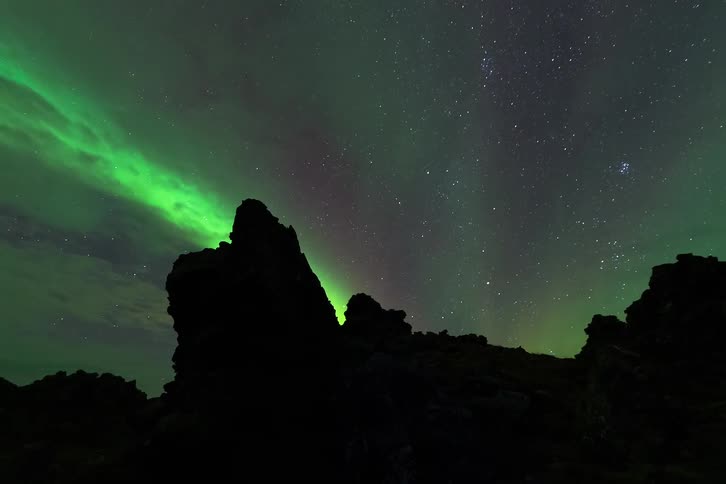 Rock formations silhouetted beneath green northern lights and a starry night sky
