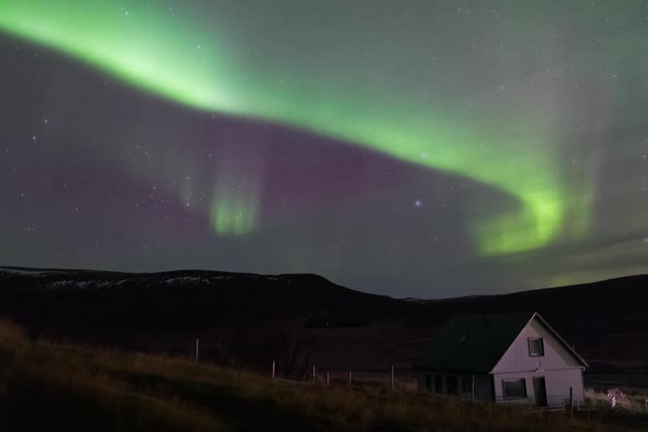 Northern lights above an isolated house in a rural area beneath a starry night sky