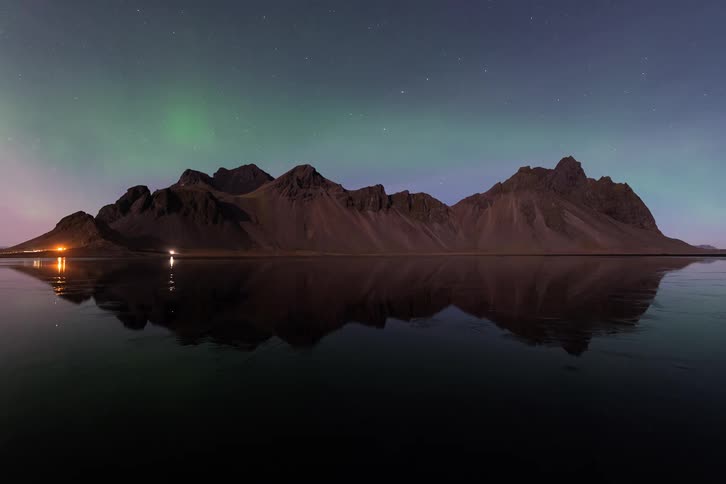 Mountains reflected in a calm lake with subtle northern lights in the night sky
