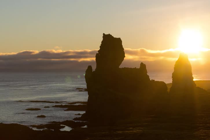 Sunset behind coastal rock formations with the ocean in the background and clouds on the horizon