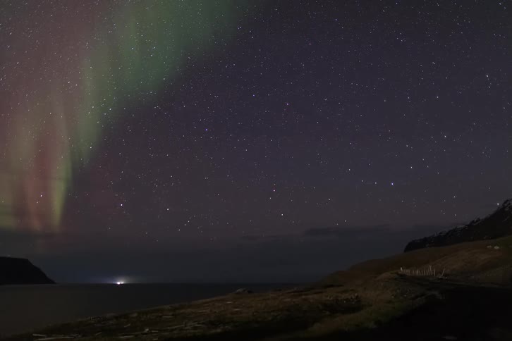 Northern lights stretching across the night sky above a dark coastal landscape