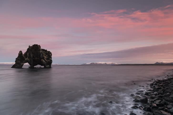 Rock formation in the water off the coast as waves roll into shore and clouds move across the sky