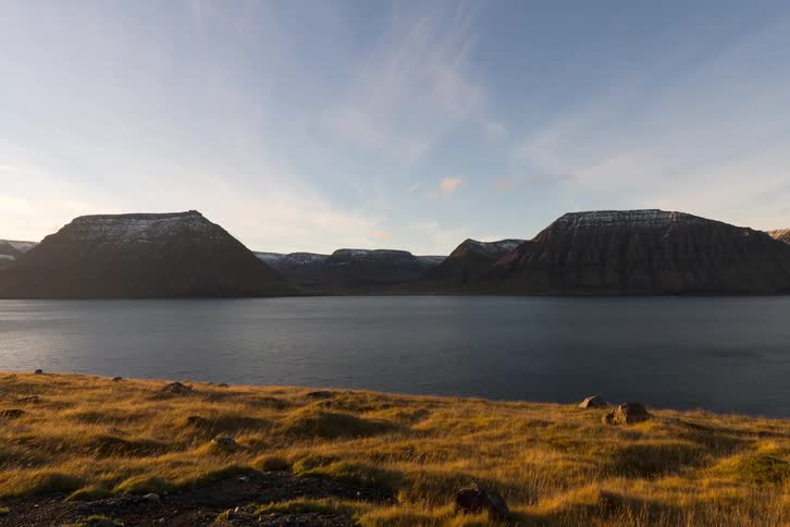 Calm lake surrounded by mountains and grassy field beneath a clear sky