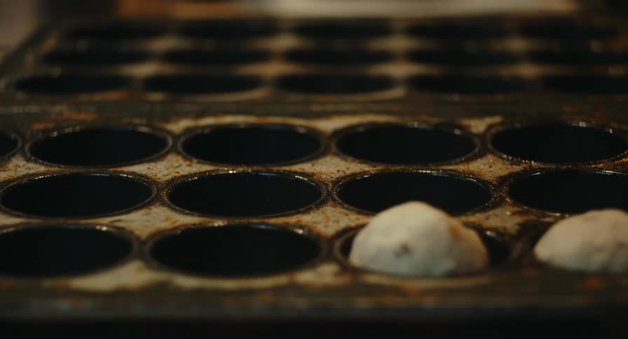 Hand placing dough into a metal tray with aligned cavities for food preparation