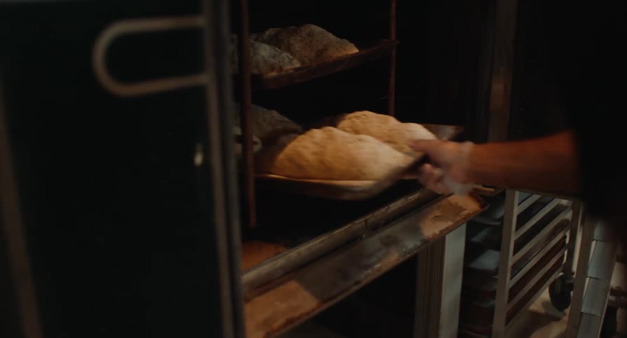 A person putting loaves of bread into an oven