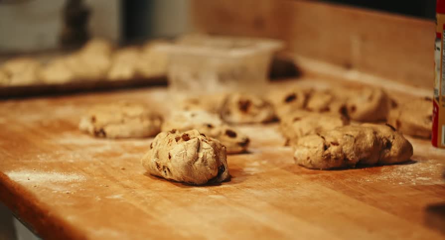 Fresh dough portions rest on a floured wooden workbench during bread preparation in a bakery kitchen