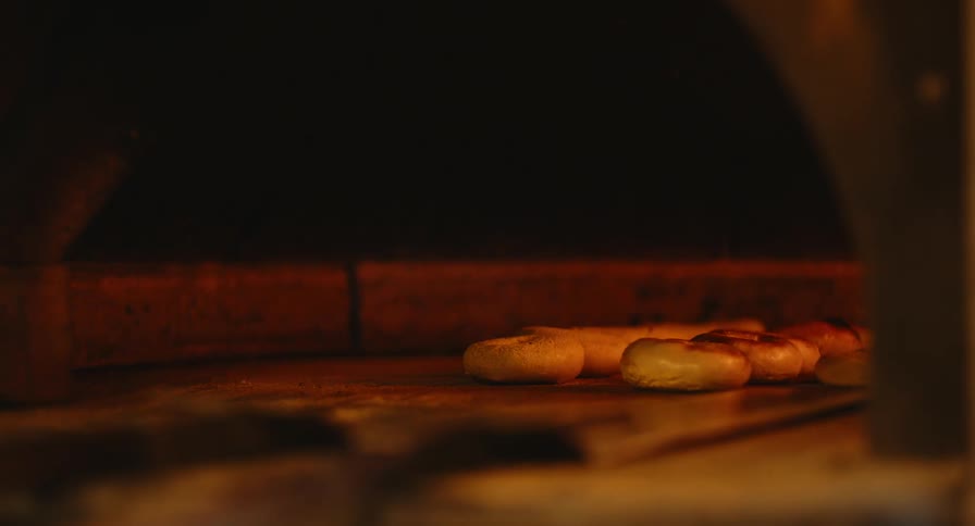 Baker puts a tray of bagels in the oven next to the tray already baking