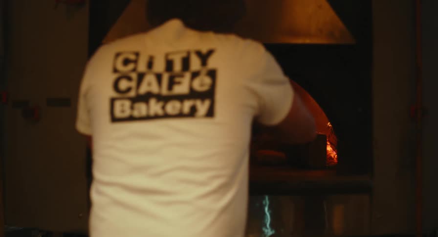 A chef stands in a kitchen baking pizza in a traditional wood fired oven