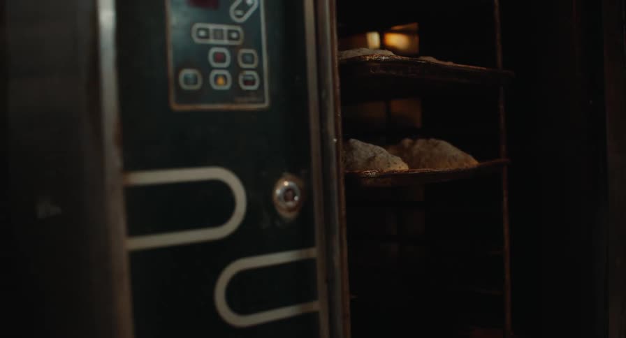 A baker slides trays of dough into an industrial oven inside a commercial kitchen