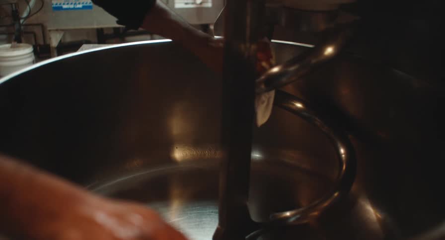 Industrial mixer in operation with dough being manually handled inside a metal bowl
