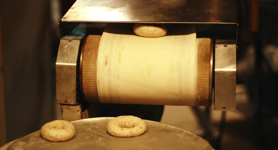 An industrial machine shapes dough into round pastries inside a commercial bakery